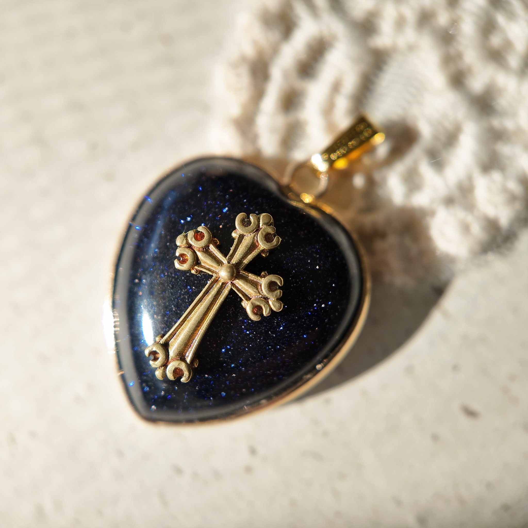 The "Galactic Faith" cross necklace by The Character Arc, featuring a sparkling blue goldstone center and a vintage antique bronze cross on a gold chain.