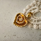 The "Sunset Vortex" sculptural gold pendant necklace by The Character Arc, featuring a fluid, ribbon-like pendant with a deep vintage gold finish on a delicate chain.