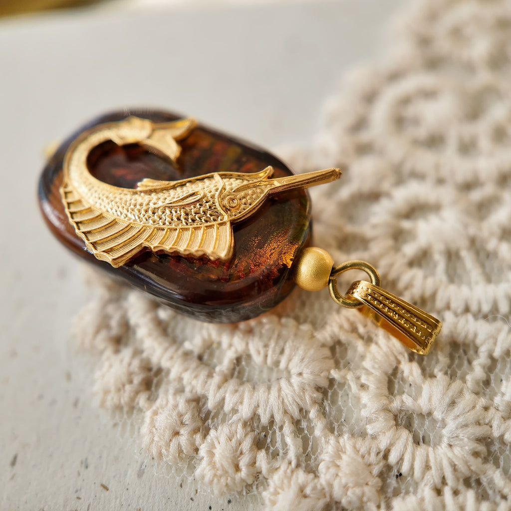 An angled view of the "Leaping Wanderer" artisan charm, highlighting the layered construction of the upcycled vintage brass and polished art glass components.