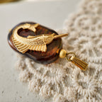 An angled view of the "Leaping Wanderer" artisan charm, highlighting the layered construction of the upcycled vintage brass and polished art glass components.