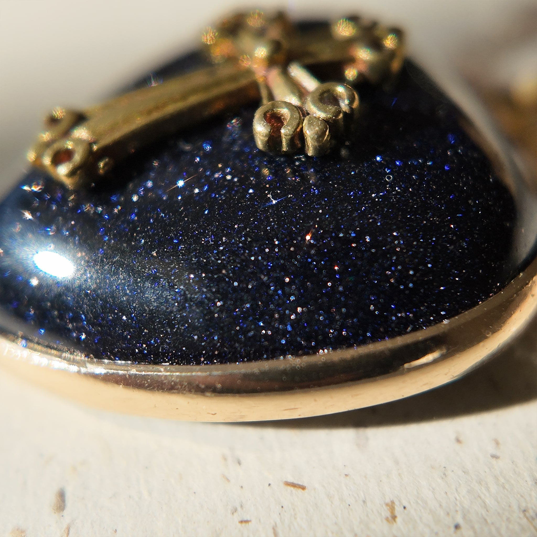 A close-up of the "Galactic Faith" pendant, showcasing the glittering galaxy-like effect of the blue goldstone against the matte, weathered patina of the bronze cross.