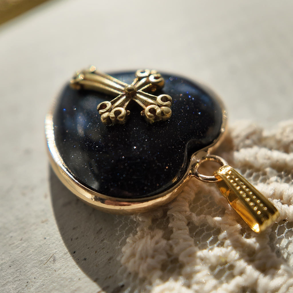 An angled view of the "Galactic Faith" celestial gothic pendant, highlighting the layering of the gold bezel, sparkling stone, and vintage cross component.