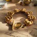 A close-up of the Anne Klein Power Dressing bracelet, showcasing the sculptural, architectural knot links and the sophisticated, non-reflective matte gold finish.