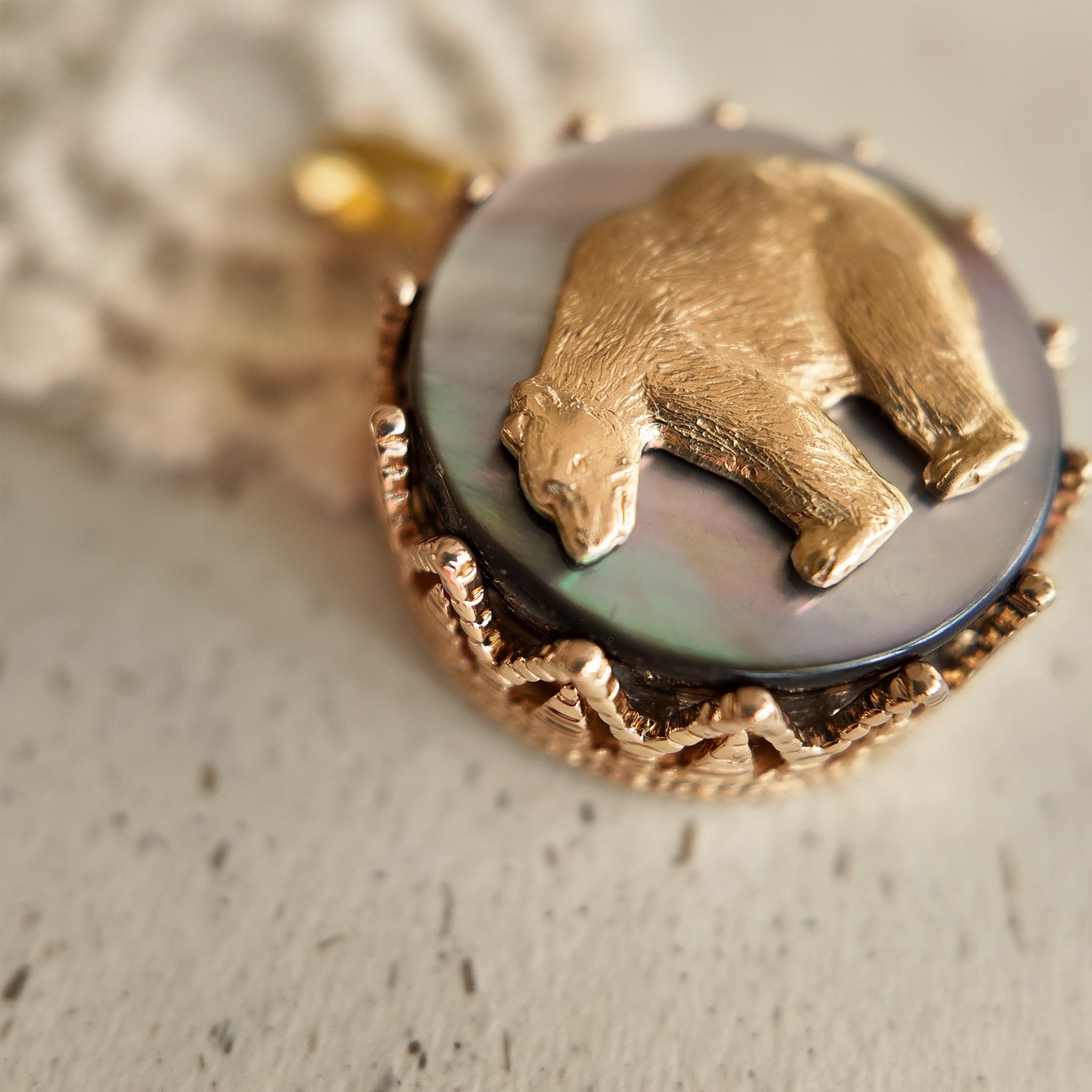 A close-up of a mythological bear pendant, showing the detailed vintage brass bear seemingly walking across a night sky of reflective Black Mother-of-Pearl.