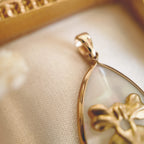 Close-up detail of the vintage brass bow and dangling heart charm, showing added movement and intricate design.