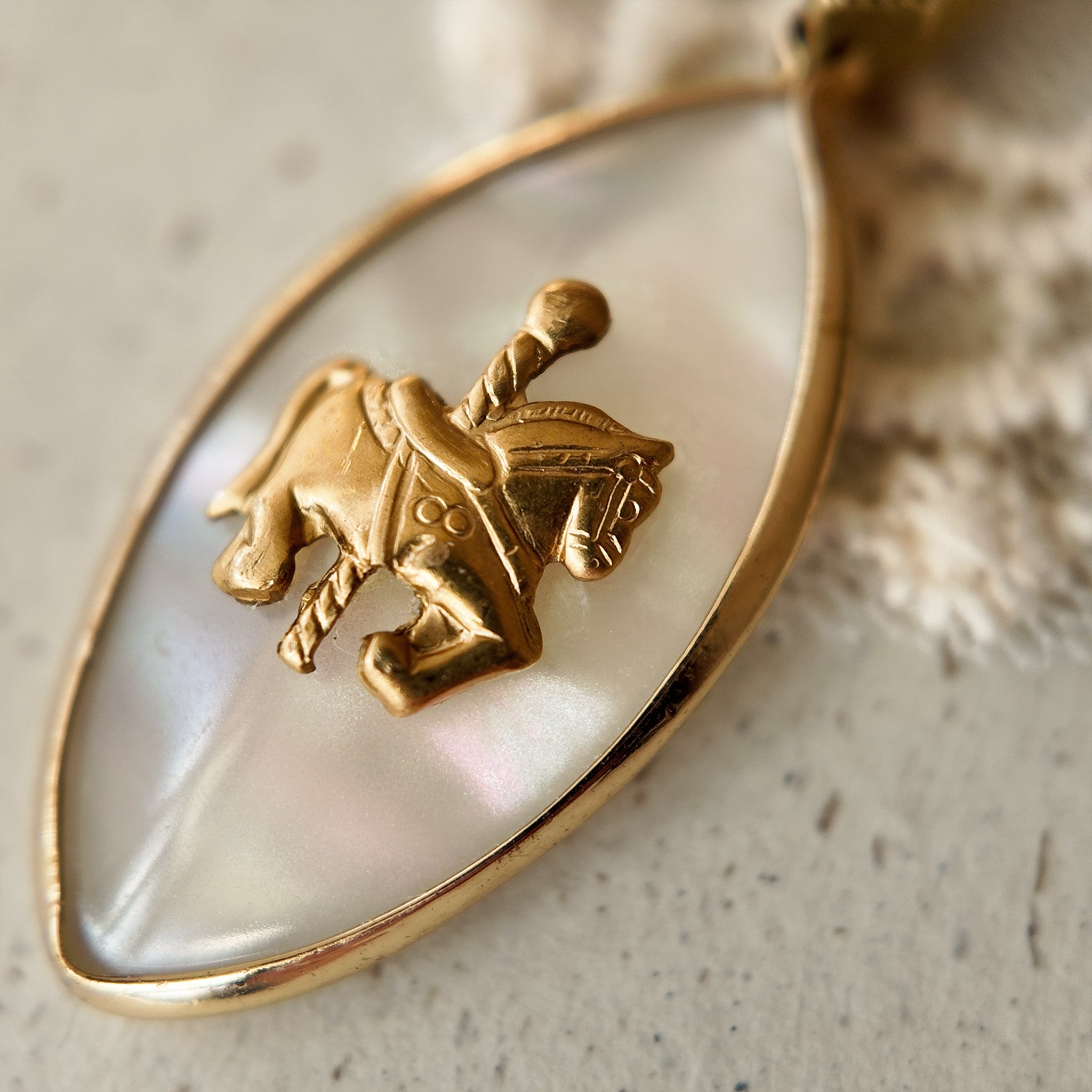 A close-up of a whimsical horse pendant, showing the detailed vintage brass carousel horse seemingly floating on a dreamy, reflective Mother-of-Pearl background.