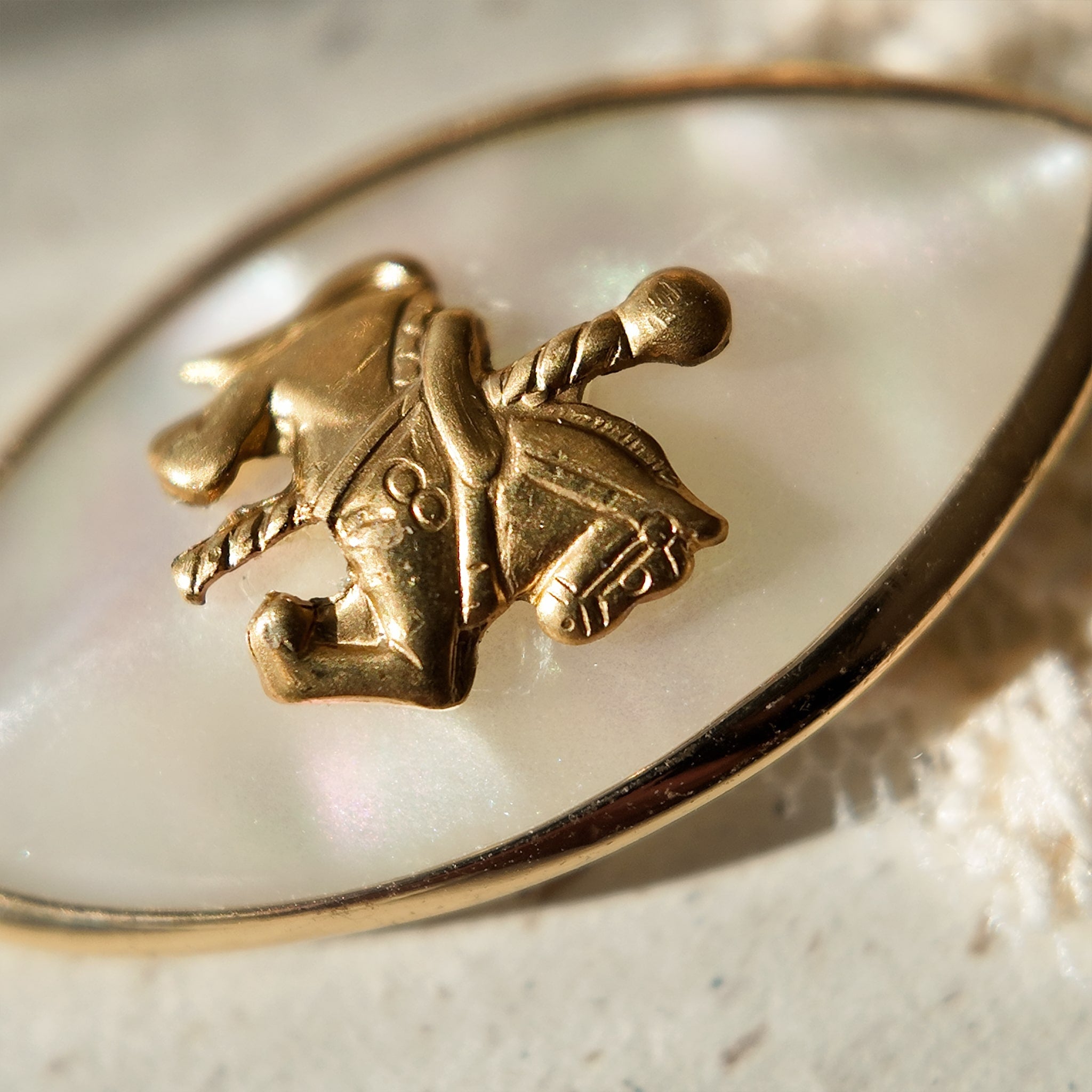 A close-up of a whimsical horse pendant, showing the detailed vintage brass carousel horse seemingly floating on a dreamy, reflective Mother-of-Pearl background.