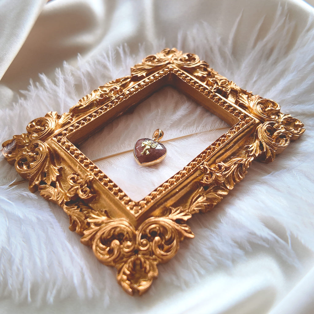 An angled view of the artisan charm, highlighting the detailed, mid-flight pose of the brass Cupid and the smooth, gold-plated bail.