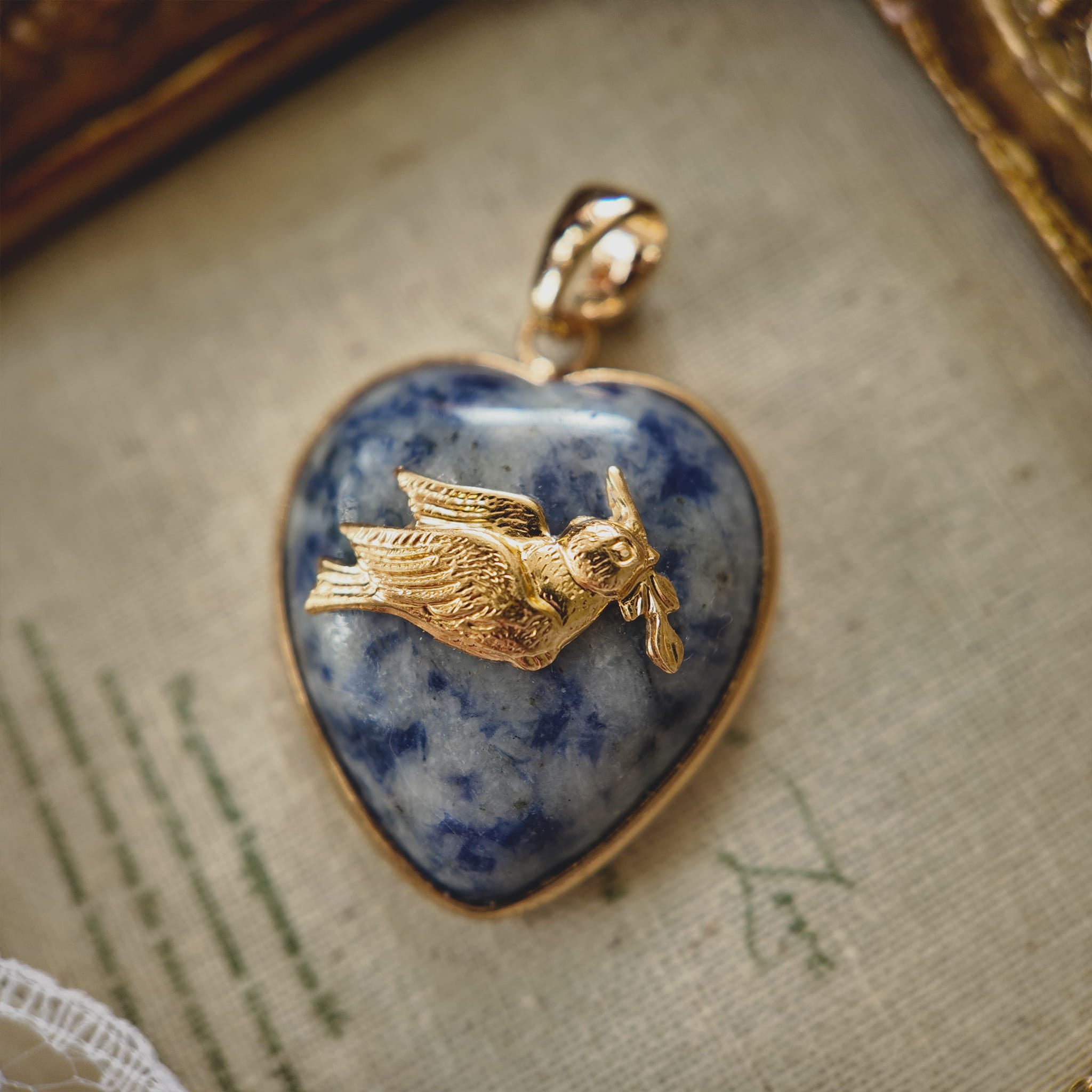 Close-up detail of the vintage brass dove carrying an olive branch charm on a natural stone background.