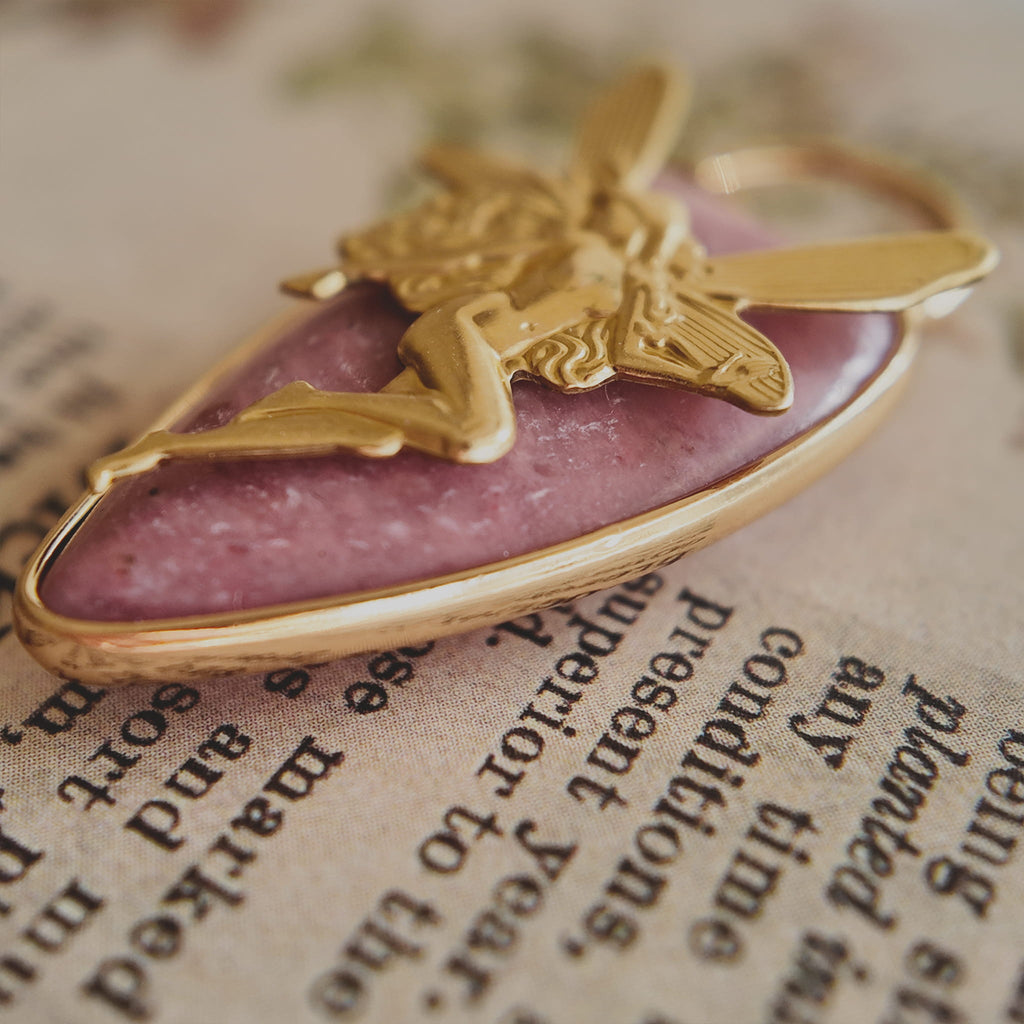 An angled view of the artisan charm, highlighting the delicate, detailed wings of the brass fairy and the smooth, gold-plated bail.