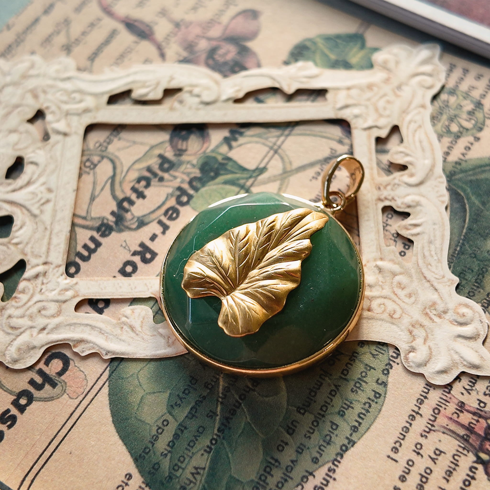 An angled view of the artisan charm, highlighting the textured, tapered shape of the brass leaf and the smooth, polished surface of the Green Aventurine, with its gold-plated bail.