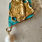 A close-up of a unique bird pendant necklace, showing the detailed vintage brass magpie perched on a branch, overlaying a natural green stone with matrix.