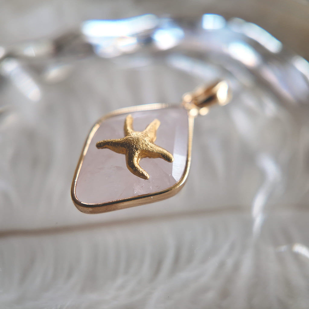 An angled view of the artisan charm, highlighting the detailed texture of the brass starfish "clinging" to the quartz surface, and the smooth, gold-plated bail.