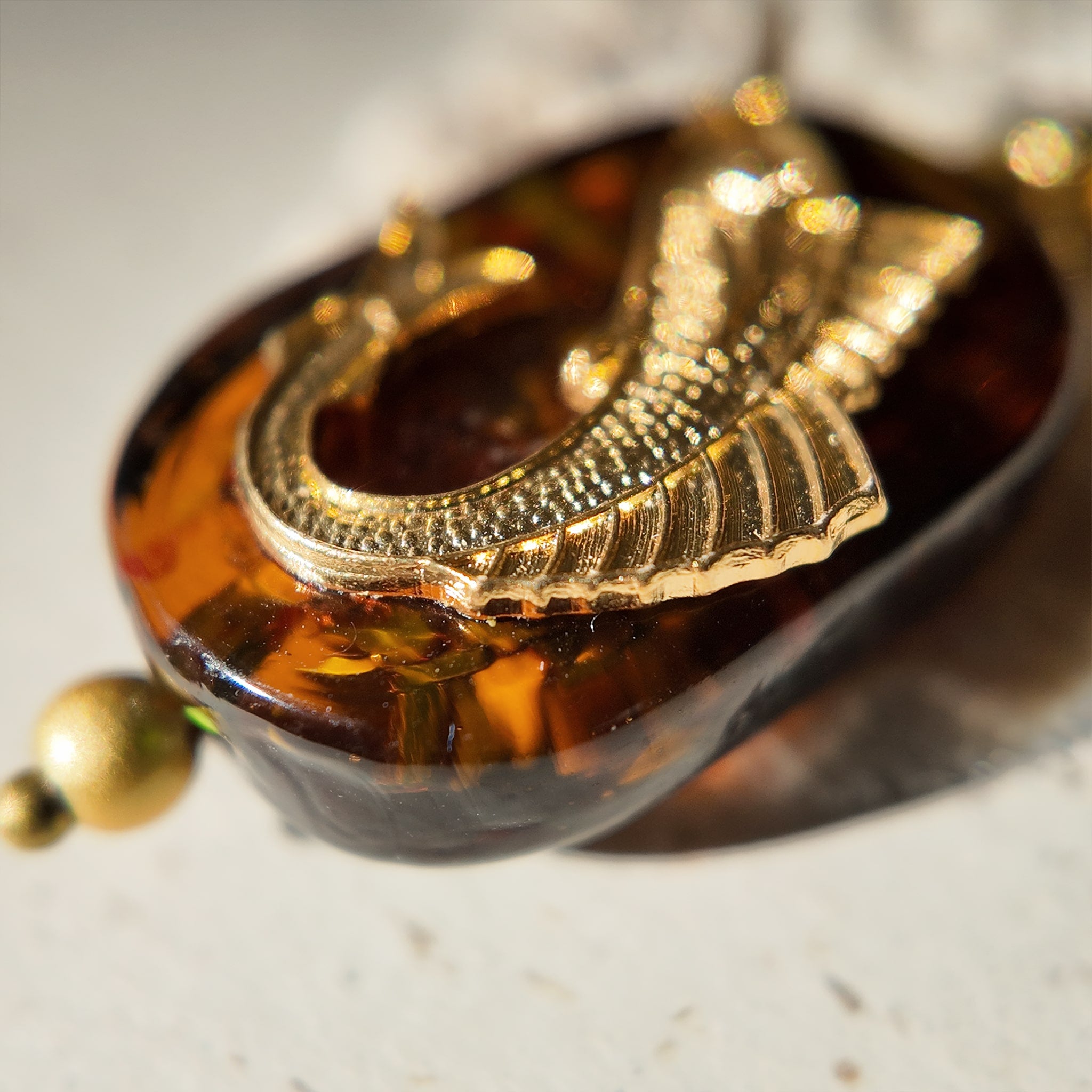 A close-up of a unique fish charm, showing the detailed vintage brass tuna appearing to leap from a sea of amber art glass with blue and green swirls.