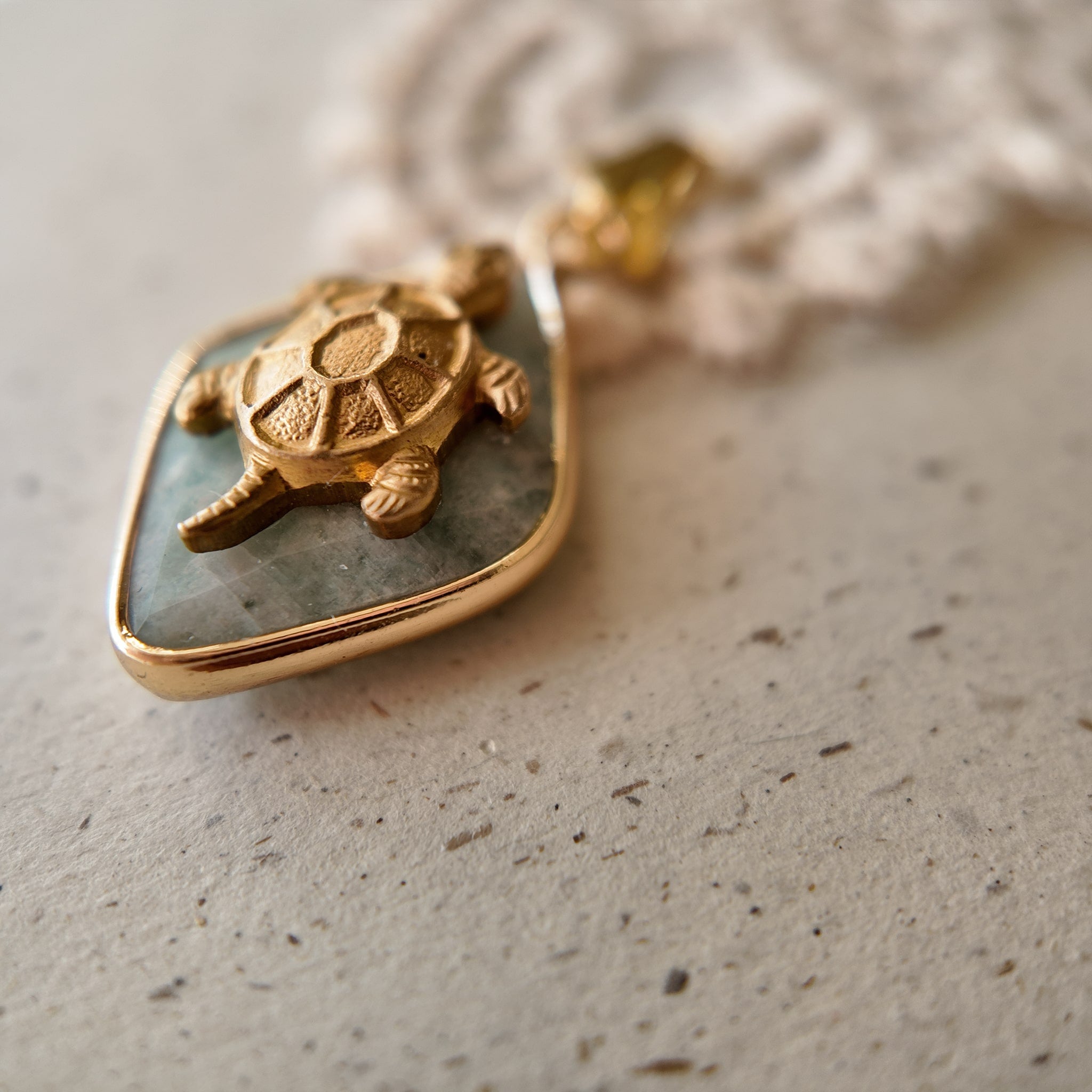 An angled view of the nature totem charm, highlighting the detailed, textured shell of the brass turtle and the smooth, gold-plated bail.