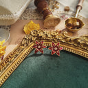 The vintage Avon Christmas earrings styled next to a mug of hot cocoa to emphasize their "cozy fireside" aesthetic and their identity as a perfect festive gift.