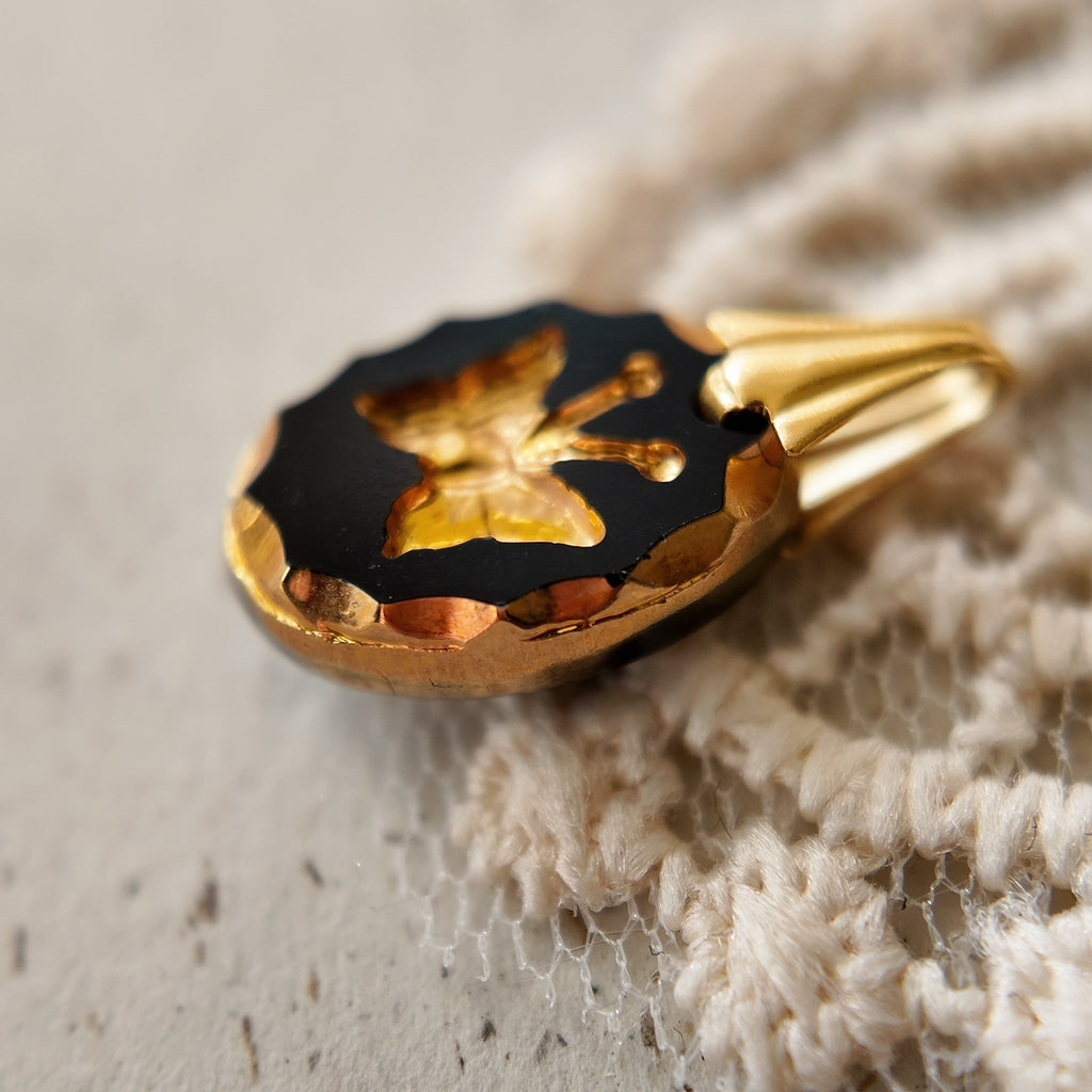 A close-up of a minimalist goth pendant, showing the detailed gold gilded butterfly intaglio carved into the jet-black vintage German glass.